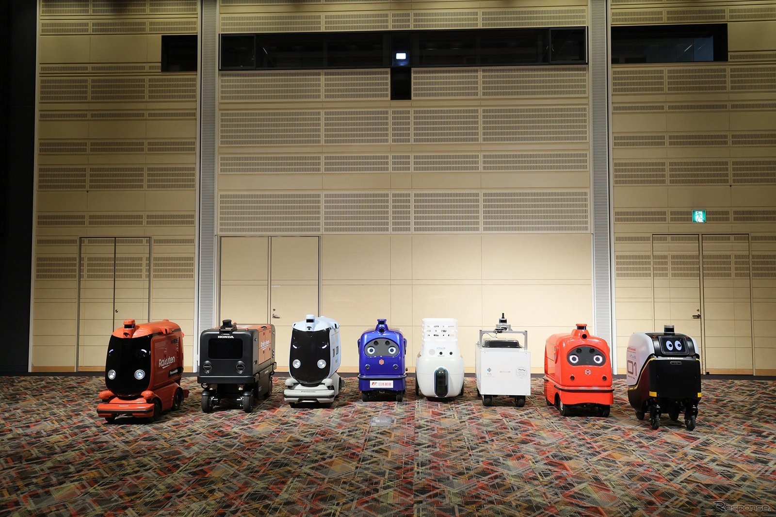 ロボットデリバリー協会各社の自動配送ロボット：向かって右から川崎重工業、ZMP、TIS、ティアフォー、日本郵便、パナソニック、本田技研工業、楽天グループ