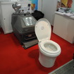 加サンコール・インダストリーズ社のバイオトイレ「エンバイロレット」。後ろにある装置で排泄物を分解して堆肥にする（「スマートエネルギーWeek2013」）