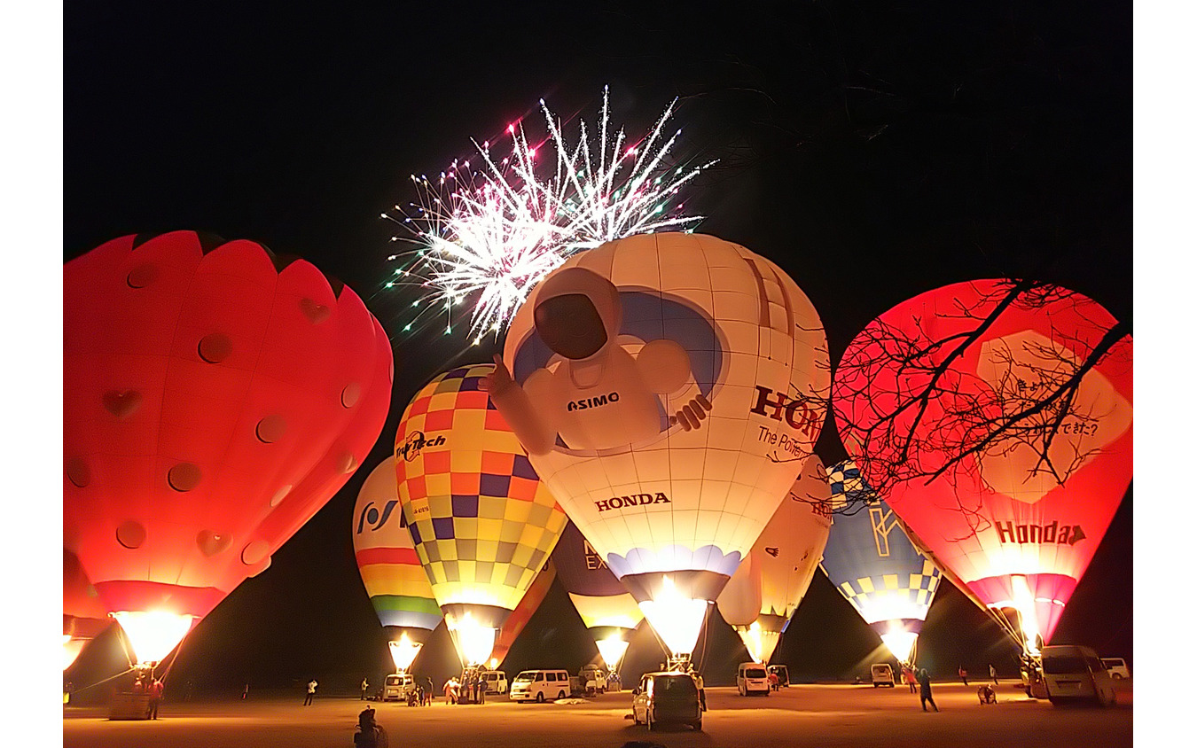熱気球ホンダグランプリ2022最終戦、渡良瀬バルーンレース2日目夜に行われたファン向けイベント「バルーンイリュージョン」。バーナーを吹かして熱気球を光らせ、背後では打ち上げ花火が結構盛大に上がる。