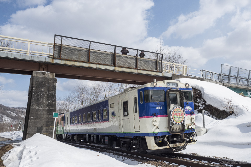 清水沢～鹿ノ谷間を行く夕張行き列車。オーバークロスしている橋は、1975年に廃止された私鉄の夕張鉄道が使用していたもので、夕張支線の廃止により廃線跡がクロスする珍しい場所となった。2019年3月30日撮影。