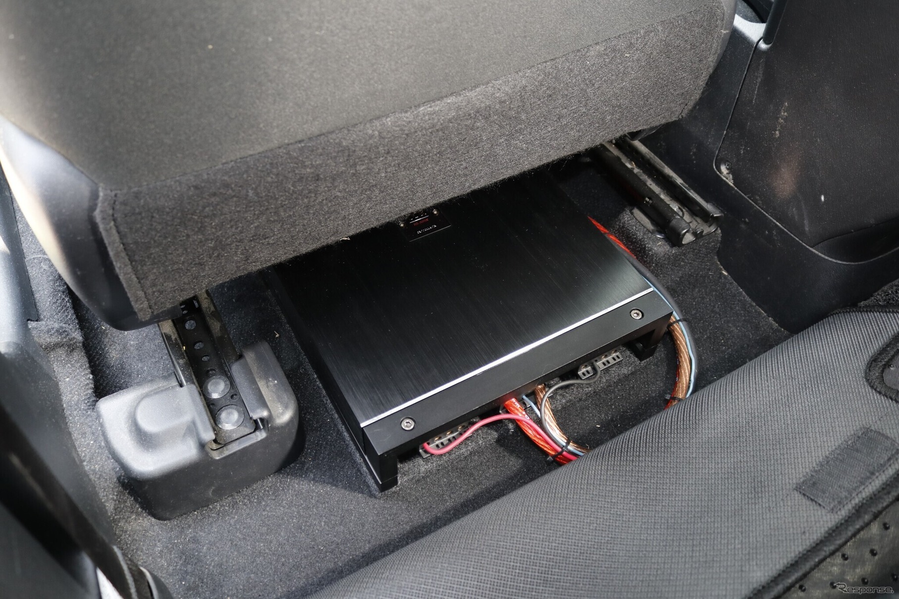 運転席／助手席ともにパワーアンプのサイズは完全には収めきれず、後部座席の足もとスペースにせり出しているのがわかる。