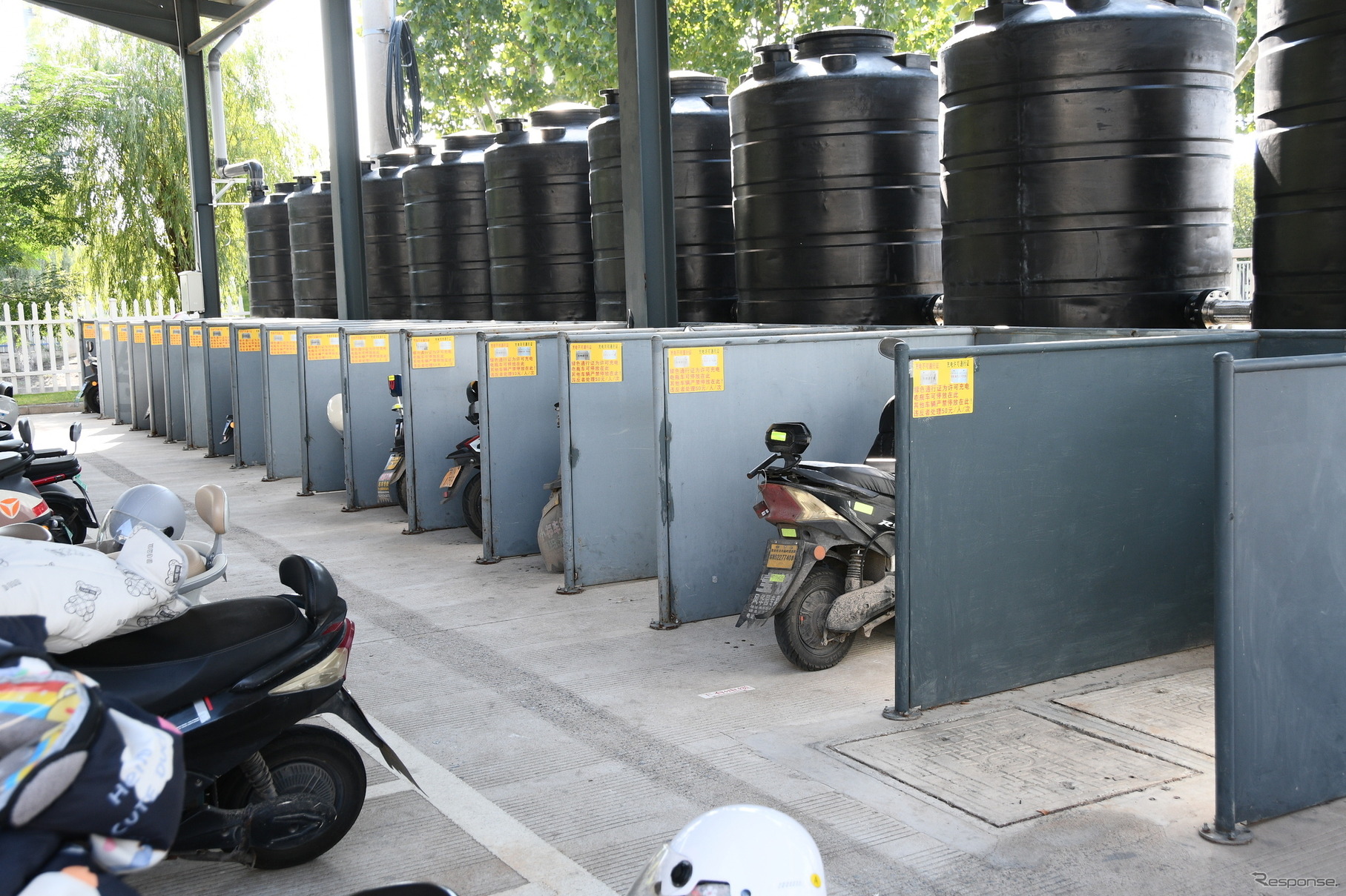 通勤用電動スクーターの充電ステーション。通勤距離が遠い人に充電の優先権がある。黒いタンクは雨水用
