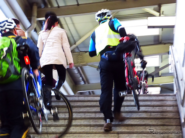 自転車を担いで階段を昇り、モノレール乗り場へと向かう参加者たち（11月30日、千葉モノレール実証実験「サイクル＆モノレール」）