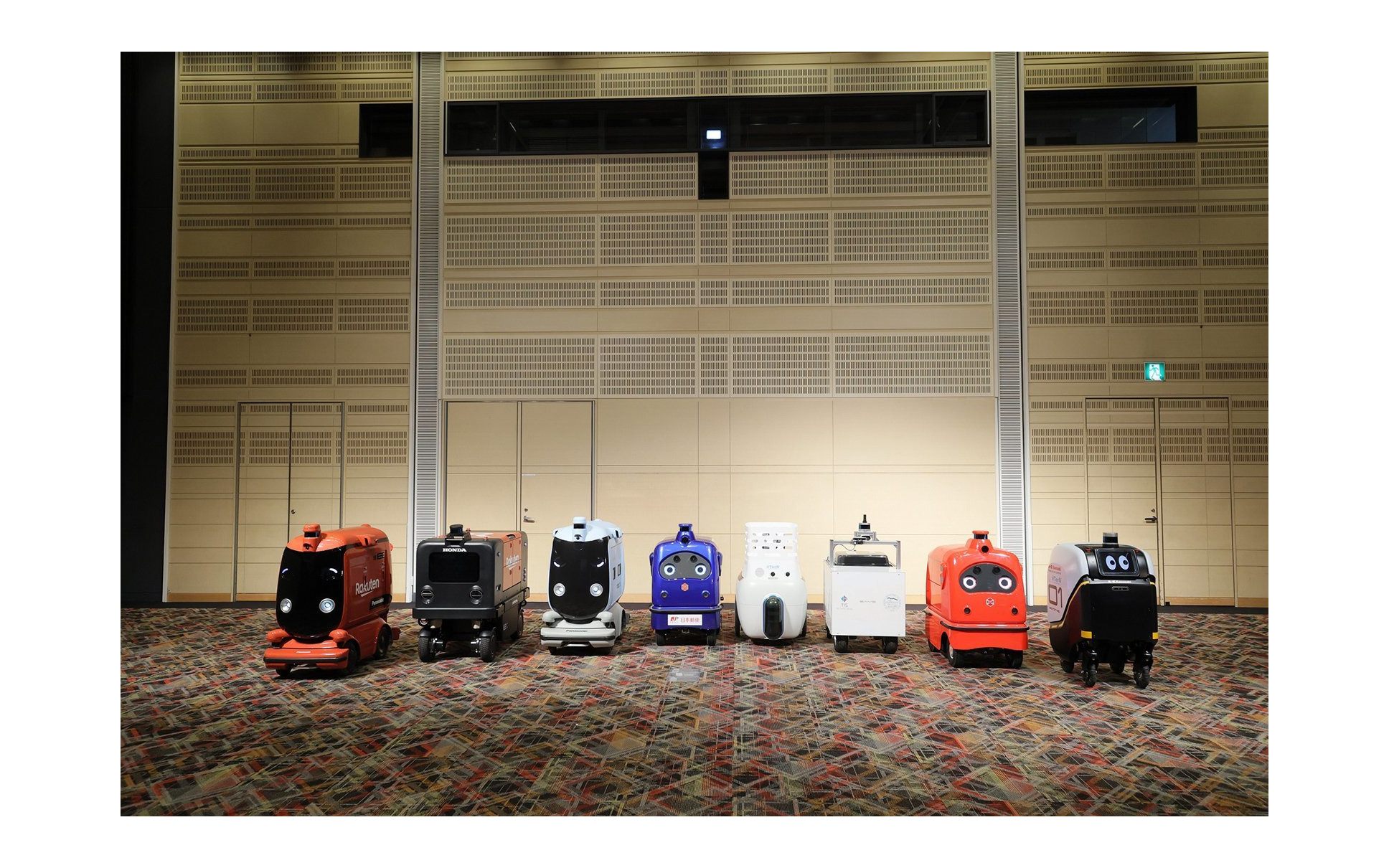 ロボットデリバリー協会各社の自動配送ロボット：向かって右から川崎重工業、ZMP、TIS、ティアフォー、日本郵便、パナソニック、本田技研工業、楽天グループ