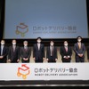 ロボットデリバリー協会発足式：向かって右から石田正俊（川崎重工業）、龍健太郎（ZMP）、油谷実紀（TIS）、加藤真平（ティアフォー）、金子道夫（日本郵便）、村瀬恭通（パナソニック）、板井義春（本田技研工業）、安藤公二（楽天グループ）