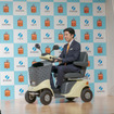 経済産業大臣政務官・佐藤啓氏が電動車いすに乗って登場。