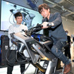 実際にヤマハ発動機がバイクの開発現場で使用するシミュレータ『MOTOLATOR』を世界初公開。デザイナーの渡辺さん（左）にレクチャーを受ける筆者・青木タカオ（右）