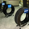 手前からリトレッドの台タイヤ（磨り減ったタイヤ）、トレッドゴムを削り取ったバフ工程後のタイヤ、クッションゴム貼り付け後のタイヤ。