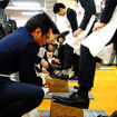 コロンブスの新人と社員が握手を交わし、先輩が手本を見せるかたちで新人の靴をみがき上げると、こんどは社員のアドバイスを聞きながら、新人たちが先輩の靴をみがいた（4月1日、コロンブス「靴みがき入社式」）